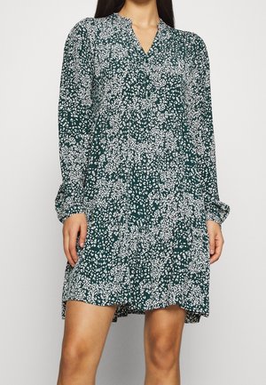 Dunkelgrünes Kleid mit einem floralen weißen Muster, langen Ärmeln, einem Stehkragen und einem leicht ausgestellt geschnittenen Saum. Leichter Stoff.