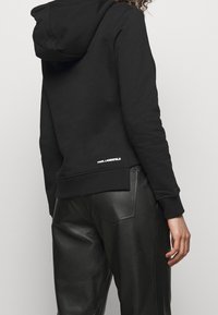 Černá mikina s kapucí vyrobená z měkké látky, s žebrovaným lemem a manžetami, s logem "KARL LAGERFELD" na dolní části zad.