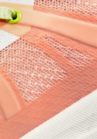 Gros plan sur un détail d’une chaussure de sport en mesh rose et en caoutchouc avec un œillet vert et un lacet blanc sur une surface blanche texturée.
