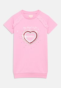 Rózsaszín pólóruha fodros ujjakkal, szív motívummal flitterekkel, alatta az "a szívem a GUESS-ért dobog" szöveggel.