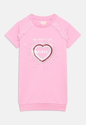 Rózsaszín pólóruha fodros ujjakkal, szív motívummal flitterekkel, alatta az "a szívem a GUESS-ért dobog" szöveggel.