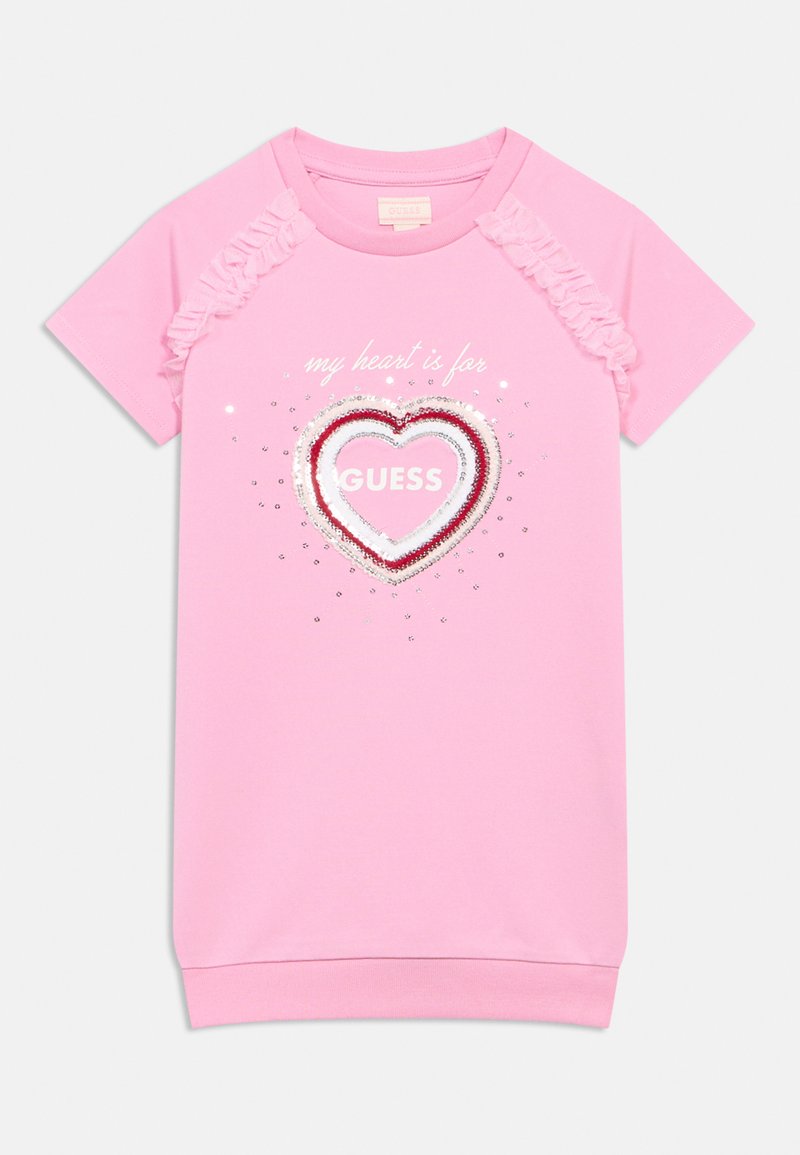 Rózsaszín pólóruha fodros ujjakkal, szív motívummal flitterekkel, alatta az "a szívem a GUESS-ért dobog" szöveggel.