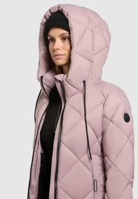 Giacca trapuntata leggera rosa chiaro con un ampio cappuccio, lacci neri e cerniera laterale. Presenta una toppa rotonda nera con logo sulla manica.