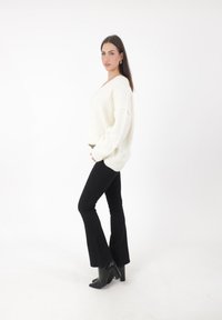 Pull crème en maille épaisse avec une coupe décontractée, associé à un jean noir évasé et des bottines noires à talon bloc.