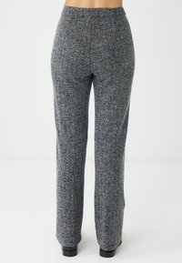 Pantalon à motif chevrons gris avec un tissu extensible et texturé. Design à jambes larges et taille élastique, avec une finition lisse.