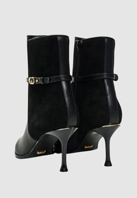 Stivaletti neri alla caviglia caratterizzati da una combinazione di pelle e camoscio, tacchi a spillo alti, dettagli in oro e chiusura laterale con cerniera.