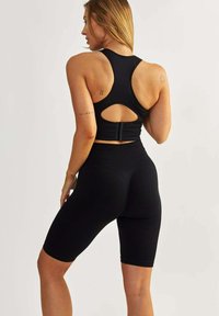 Czarny stanik sportowy z wycięciem na plecach i regulowanym zapięciem, w połączeniu z czarnymi rowerowymi szortami o wysokim stanie i żebrowanej fakturze.