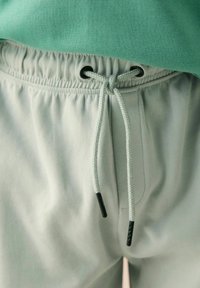 Close-up of light grey sweatpants with elastic waistband and tied drawstring under green shirt.