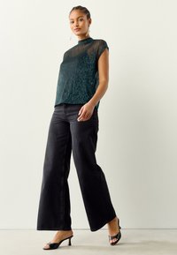 Plavižuti pleteni top s visokim izrezom, upareni s crnim trapericama širokih nogavica i crnim sandalama s potpeticom. Top ima teksturirani uzorak.