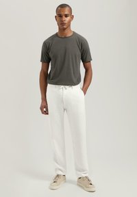 Mørk grå t-skjorte med kort erme, parret med løstsittende hvite linbukser og lyse sneakers. Minimalistisk design, uformell stil.