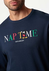 Sudadera azul marino con cuello redondo que presenta texto bordado "NAP TIME" en letras de colores y una imagen de Mickey Mouse con pantalones cortos rojos.
