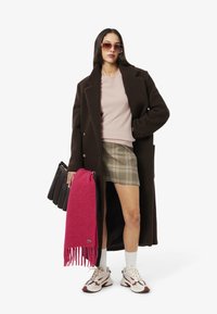 Brun ullkappa, ljusrosa tröja, rutiga kjol, rosa scarf, svart väska, vita strumpor, beige och röda sneakers, överdimensionerade solglasögon.