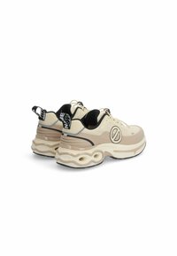 Beige sneakers met een gestructureerde bovenkant, zwarte accenten en een stevige zool met ronde uitsparingen. Vetersluiting en logo-detail zichtbaar.