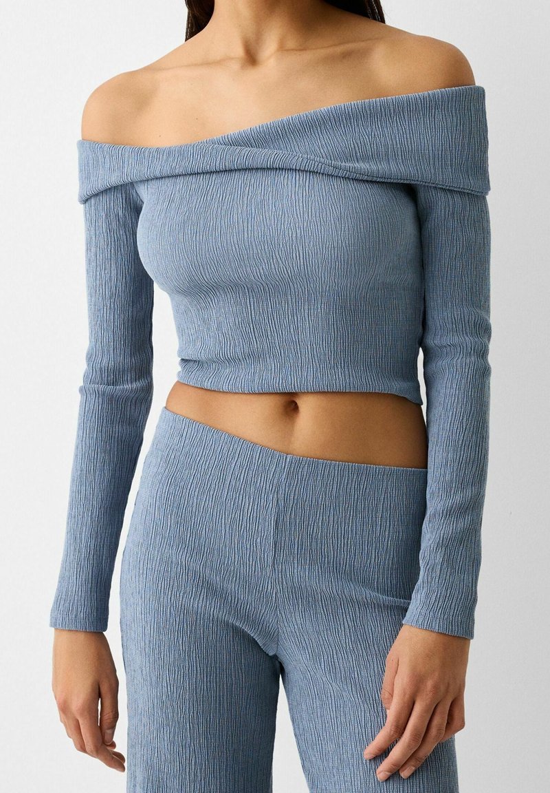 Lichtblauwe off-shoulder lange mouw top van textuur ribstof, gecombineerd met bijpassende rib geweven high-waisted broek.