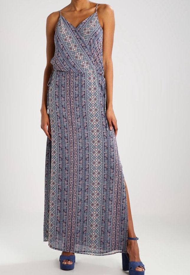 Robe maxi en tissu à motifs bleus et roses avec des rayures diagonales, des bretelles fines et une fente sur le côté. Associée à des sandales à talons bleues.