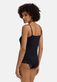 Černý top na ramínka s nastavitelnými tenkými popruhy, hladkým materiálem a propracovanými krajkovými detaily na lemu. Těsně přiléhá k tělu.