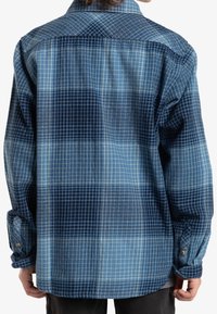 Niebieska koszula w kratę z wzorem siatki w różnych odcieniach, z długimi rękawami, mankietami na guziki i luźnym krojem, wykonana z bawełnianej tkaniny.