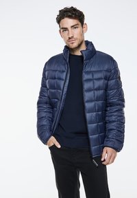 Navy quilted puffer jacket with a high collar, front zipper, and side pockets. Smooth, glossy fabric with a lightweight design.