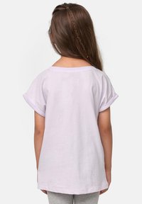 T-shirt di un leggero color lavanda con maniche corte arrotolate, un ampio scollo e una vestibilità rilassata. Tessuto uniforme senza pattern o accessori visibili.