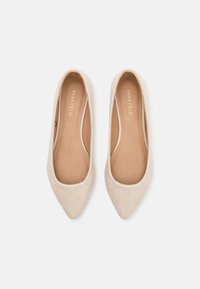Beige Lacklederballerinas mit spitzem Zehenbereich, ausgestattet mit einem gesteppten Kreuzmuster im Zehenbereich und einem glatten Innenfutter.