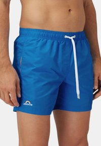 Pantaloni da bagno blu realizzati in tessuto leggero, dotati di una cintura elastica con cordino bianco e un piccolo logo con dettaglio arcobaleno.