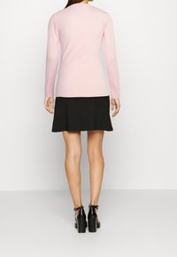 Ljusrosa långärmad topp i kombination med en svart utsvängd kjol, styllt med kraftiga svarta klacksandaler. Slät textur, enkel rund halsringning.