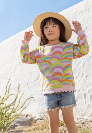 Barevná mikina s dlouhým rukávem a vzorem duha, růžový základ a volánkový lem; doplněná džínovými šortkami s krajkovým lemem.