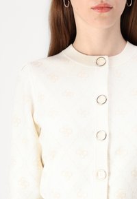 Cream cardigan with diamond pattern, featuring large silver buttons down the front, ribbed collar, and soft texture.