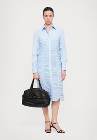Rochie cămașă albastru deschis cu textură plisată, mâneci lungi și guler. Geantă tote din piele neagră cu mânere scurte. Sandale negre cu curele.
