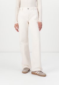 Vide benedrelser i off-white bomull, med klassisk fem-lomme design og knappe-lukking. Brukt med grå fottøy og ribbet topp.