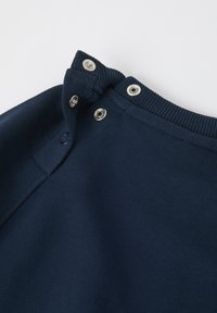 Navy blue sweatshirtin kauluksessa on hopeiset nepparit ja ribbikuvio. Lähikuva, joka näyttää ompelutiedot ja kankaan sileän pinnan.