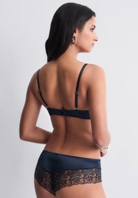 Ensemble de lingerie bleu marine composé d'un soutien-gorge en satin lisse avec des bretelles réglables et d'une culotte à dentelle, mettant en valeur des motifs floraux délicats.
