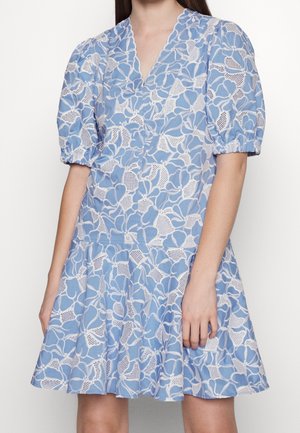 Frau trägt ein hellblaues Kleid mit weißem floralen Spitzenmuster, kurzen Puffärmeln, V-Ausschnitt und ausgestelltem Rock.