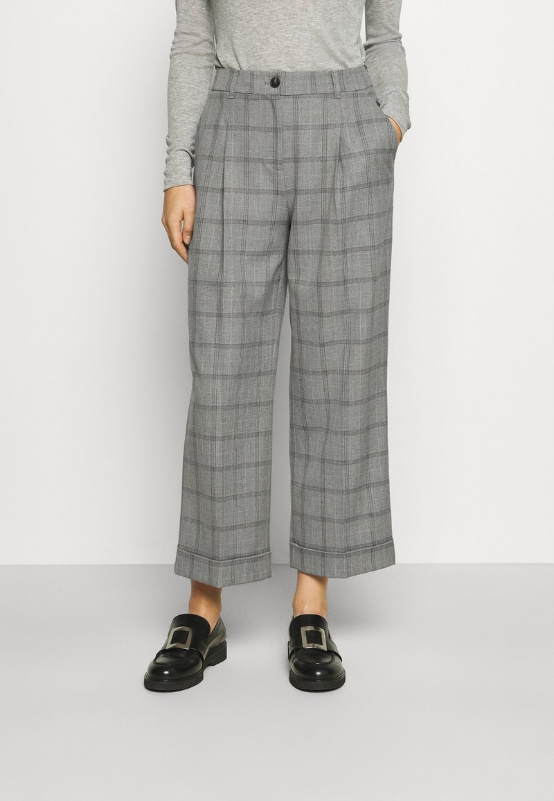 Kobieta nosząca szare szerokie spodnie w kratkę z mankietami, połączone z czarnymi loafersami z dużymi srebrnymi klamrami.