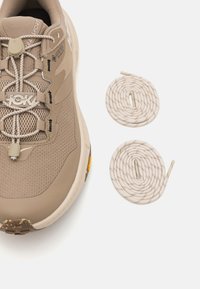 Beige lightweight sneaker with mesh and synthetic materials, featuring elastic laces, a textured sole, and two matching rounded laces.