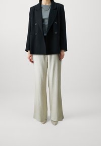 Blazer noir à double boutonnage avec de gros boutons sur un haut gris, associé à un pantalon en lin large beige clair et des talons aiguilles nude.