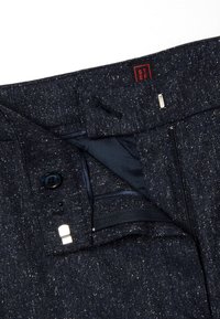 Marineblauwe broek met een gespikkelde textuur, voorzien van een knoopsluiting, ritssluiting en een interne pocketdetail. Merktag zichtbaar aan de binnenkant.