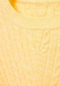 Keltainen neulepaita, jossa on resorinen pyöreä pääntie ja palmikkokuviota, pehmeä tekstuuri ja pystysuorat linjat koko kankaan läpi.