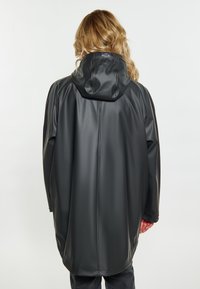 Abrigo largo, gris oscuro, impermeable y con capucha, hecho de material suave. Presenta una etiqueta de marca en el cuello y un diseño de corte holgado.