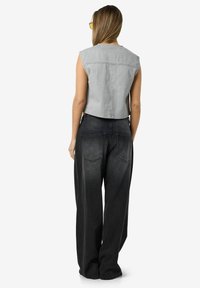 Sivi skraćeni traper prsluk s sirovim rubom, uparen s širokim crnim trapericama koje imaju stražnje džepove i izblijedjeli izgled.