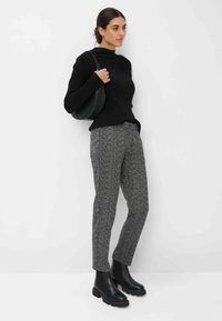 Schwarzer gerippter Rollkragenpullover, graue gemusterte Hose und schwarze klobige Stiefeletten. Zubehör beinhaltet eine runde schwarze Tasche.