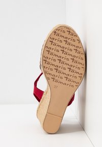 Semelle d'une sandale compensée rouge avec une bande de roulement en caoutchouc à motif comportant le nom de la marque Tamaris et la taille 37 indiquée sur la semelle.