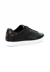 Sneaker basse en cuir noir avec motifs géométriques en relief, languette de talon marron à motifs, lacets noirs et semelle en caoutchouc blanche.