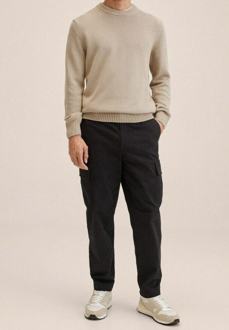 Beige Strickpullover mit rundem Kragen, kombiniert mit schwarzen Cargo-Hosen mit Taschen und hellen Sneakers mit strukturiertem Design.