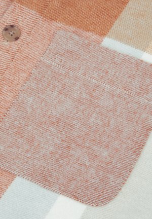 Geruite textiel met een zachte, perzikkleurige zak met een gladde textuur. Knopdetail in een lichte bruine kleur.