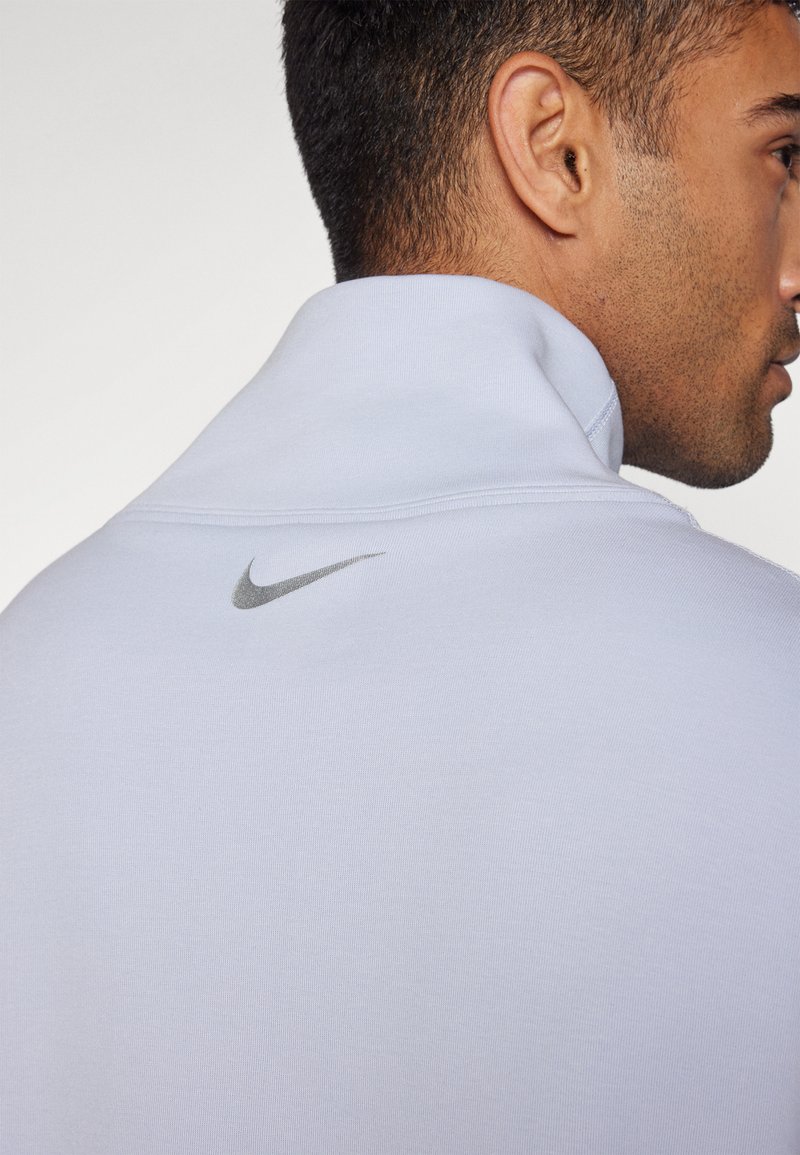 Pullover sportivo azzurro chiaro con colletto alto. Presenta un tessuto testurizzato e un piccolo logo metallico argento sul retro.