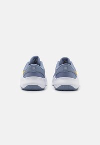 Zapatillas deportivas en azul claro con parte superior de malla y acentos amarillos. Suela blanca redondeada con una suela exterior texturizada para mayor agarre. Diseño simétrico y talón acolchado.