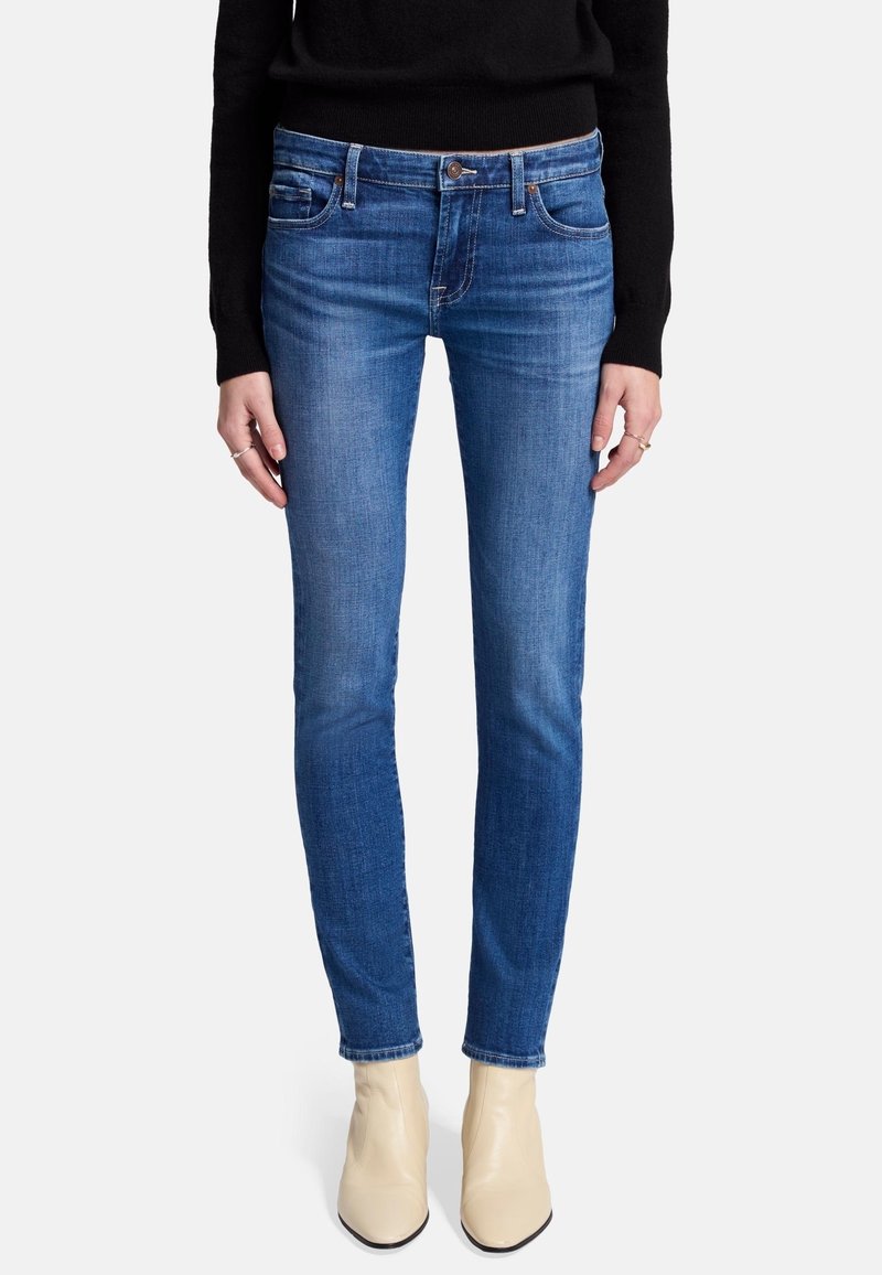 Skinny blue jeans made of denim, featuring a mid-rise waist, five-pocket design, and subtle fading. Worn with cream ankle boots.