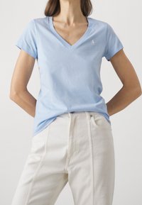 Ljusblå bomulls t-shirt med V-ringning och korta ärmar, prydd med en liten vit logotyp på bröstet, tillsammans med vita byxor med hög midja.