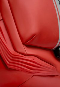 Material acolchado rojo con secciones lisas y texturizadas. Presenta formas curvas y líneas de distintas profundidades, combinadas con acentos en negro.